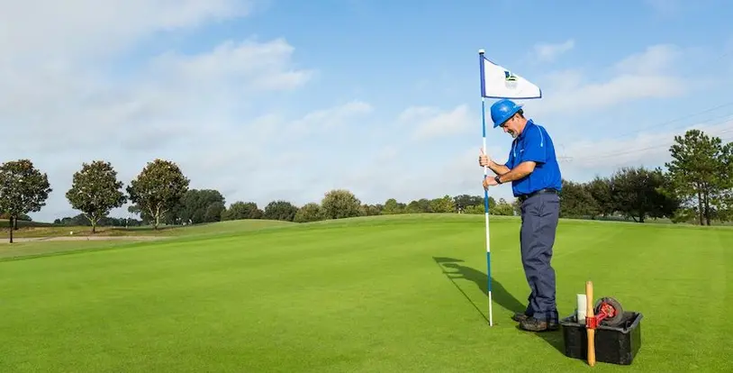 golf course maintenance crew member placing flagstick in hole